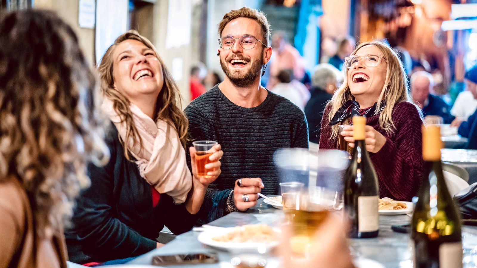 Friends laughing over drinks and plates at a shared table