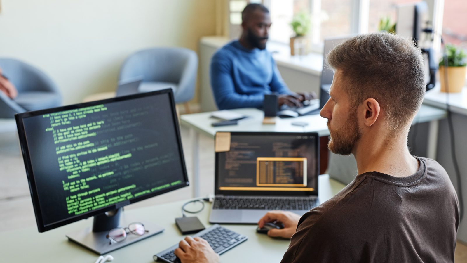 Two developers at work in a small office, code on the screens
