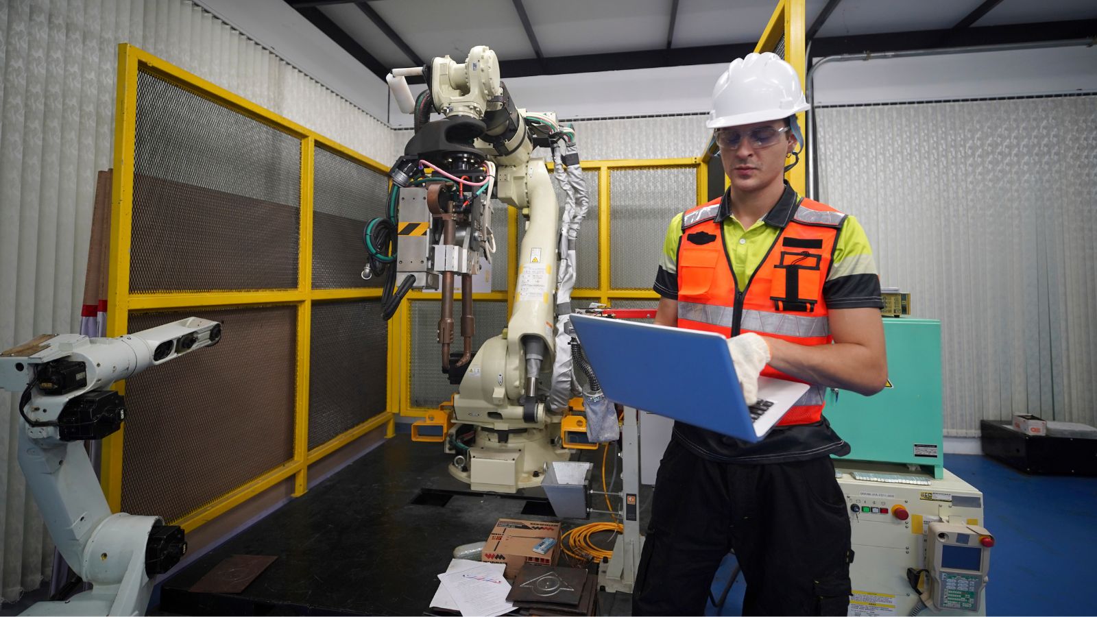 An engineer with a laptop beside an industrial robot arm in a flex-tech bay