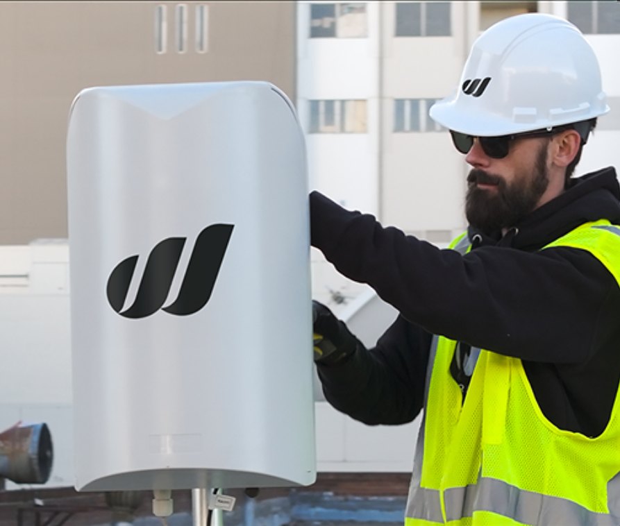 A World Mobile technician installs a small-cell antenna on a rooftop